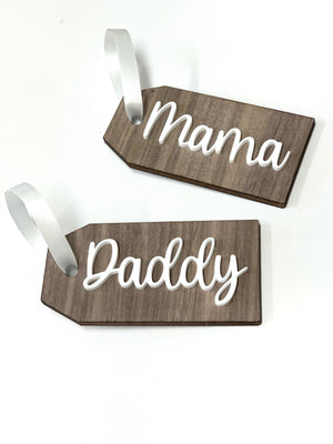 Two custom 2x4 inch wooden gift tags with white cursive names Mama and Daddy and satin ribbon loops on white background