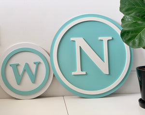 Two 3D monogram round wooden signs painted turquoise and white with raised letters W and N on white surface