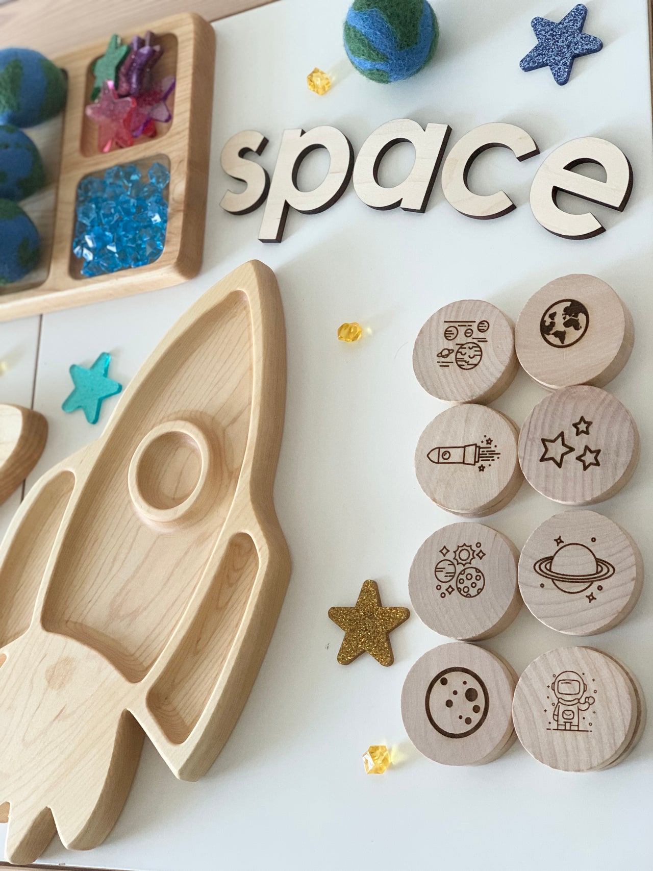 Wooden space themed memory game discs with engraved planets, rocket, astronaut, and stars next to wooden rocket tray and letters spelling space