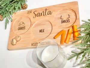 Natural wooden Santa plate with engraved sections for cookies, milk, and reindeer snacks on white background with greenery