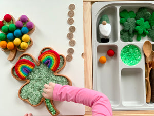 Small and large shamrock-shaped wooden sensory trays with green rice, felt balls, wooden spoons, and small felt clovers
