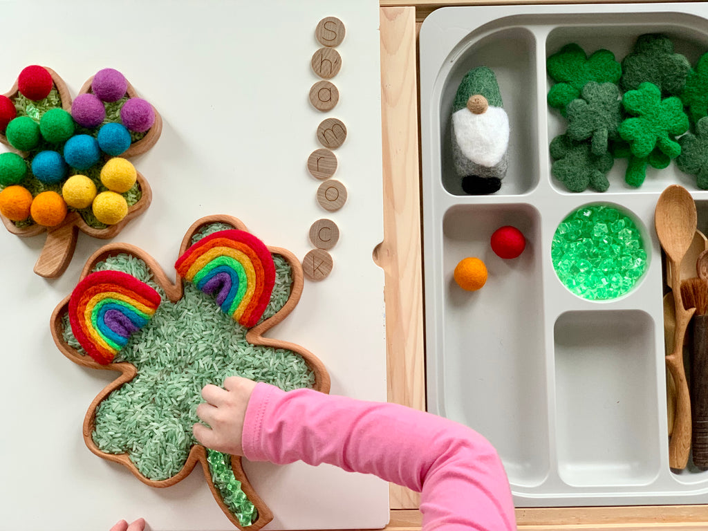 Small and large shamrock-shaped wooden sensory trays with green rice, felt balls, wooden spoons, and small felt clovers