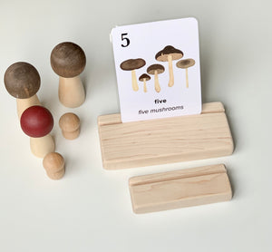 Natural wooden flash card holder with a flash card showing five illustrated mushrooms on white background