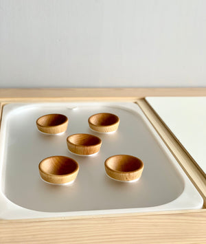 Set of five small wooden bowls placed on a white acrylic insert in a light wood tray frame