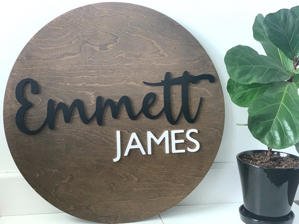 3D round wooden name sign with black cursive first name and white block last name on stained wood background
