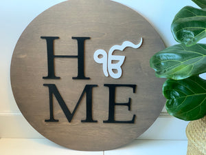 Round wooden name sign with black letters and white symbol on natural wood background next to green leafy plant