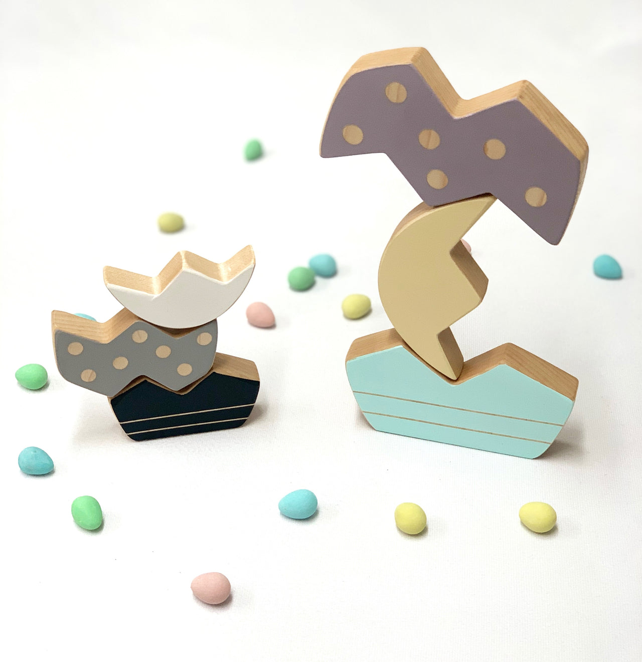 Wooden pastel Easter egg stacking toy pieces balanced in two stacks with small colorful candy eggs on white background