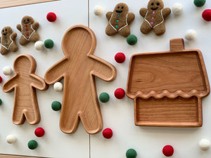 Three wooden sensory trays shaped like gingerbread people and a house surrounded by felt balls on white surface