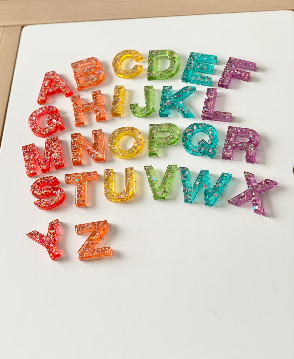 Rainbow glitter resin uppercase alphabet letters arranged on white surface in colorful gradient order
