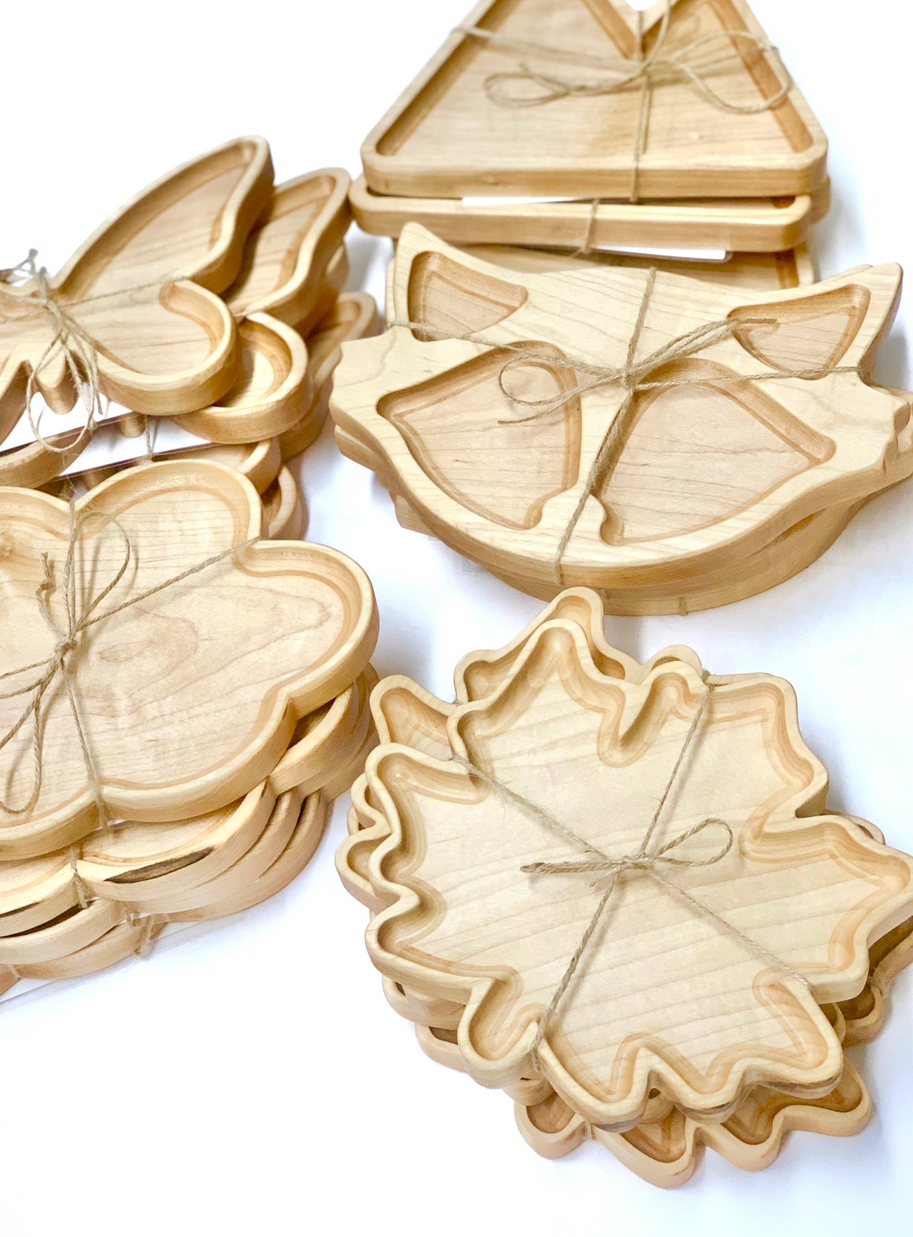 Stacks of natural wooden sensory trays shaped like fox, butterfly, leaf, and triangle tied with twine on white background