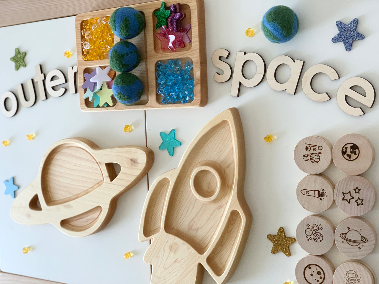 Handmade felt globe balls with wooden space-themed toys including a rocket, planet, and stamped wooden discs on white surface