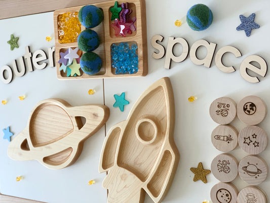 Handmade felt globe balls with wooden space-themed toys including a rocket, planet, and stamped wooden discs on white surface