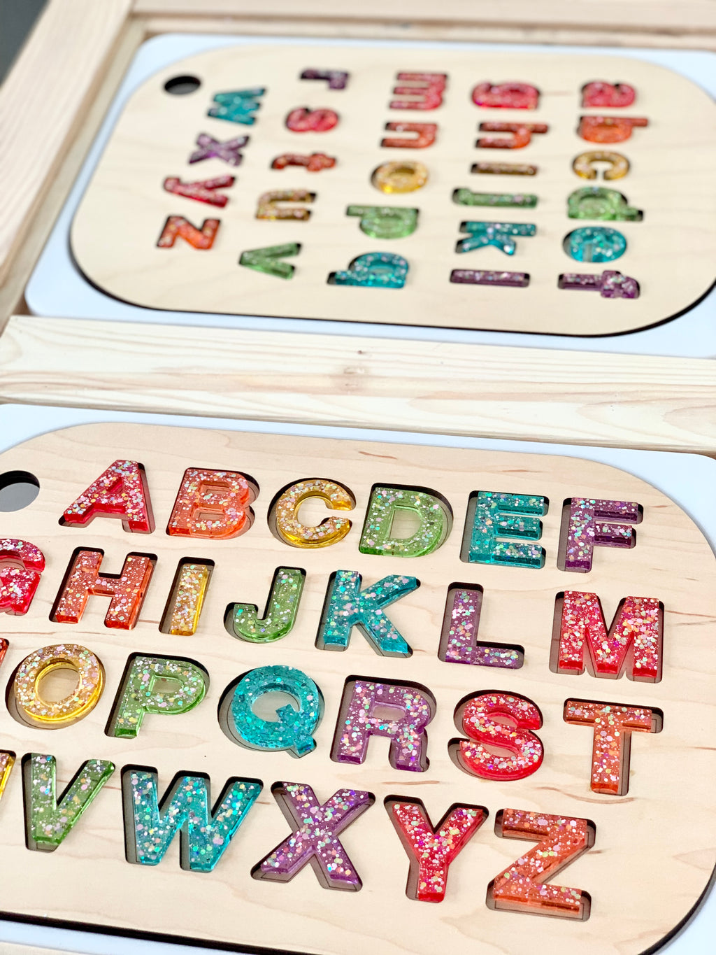 Rainbow glitter resin uppercase alphabet letters arranged on wooden board with lowercase letters on second board underneath