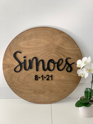 Round wooden guest book alternative sign with black cursive last name and date on natural wood grain background