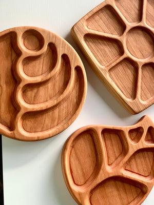Three natural wood sensory trays in sun rays, abstract round, and leaf shapes on white surface