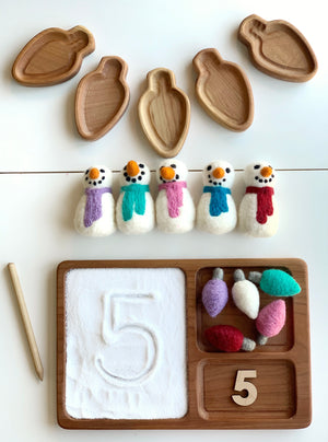 Wooden light bulb-shaped trays with felt snowmen and sensory tray holding salt, felt bulbs, and wooden number on white background