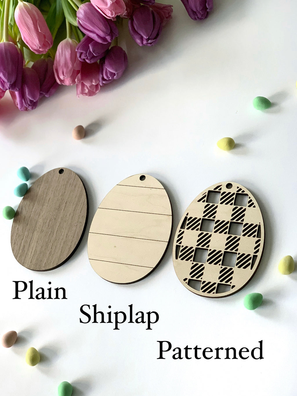 Three large wooden Easter egg name tags with plain, shiplap, and patterned designs on white surface with pastel decorations