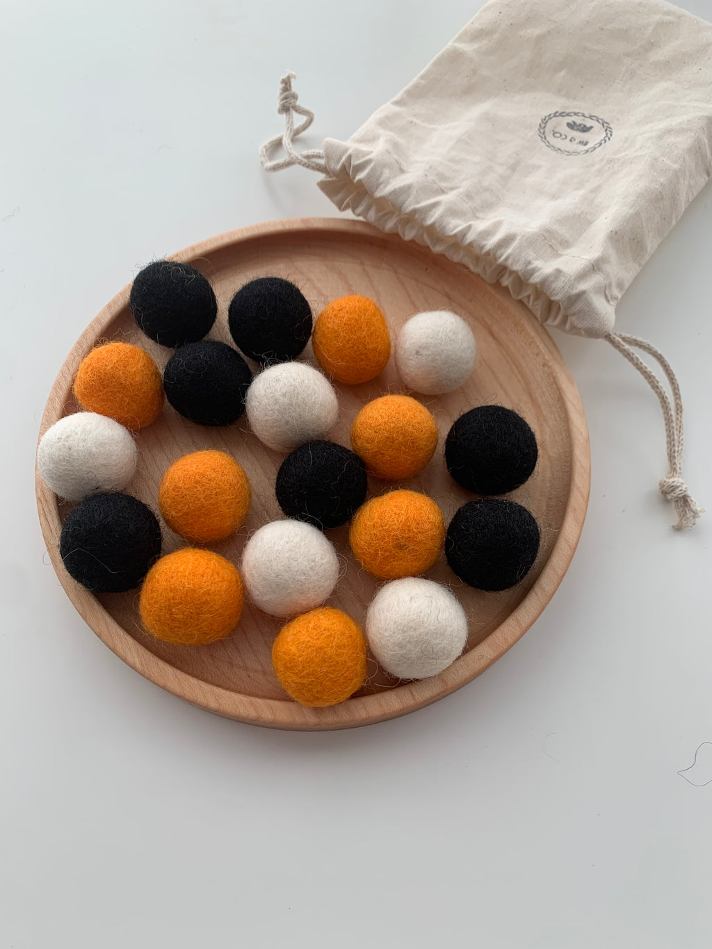 Assortment of black, orange, and white felt balls arranged on round wooden plate with cloth drawstring bag nearby