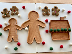Set of three natural wooden sensory trays shaped like gingerbread people and a house surrounded by felt balls and gingerbread figures