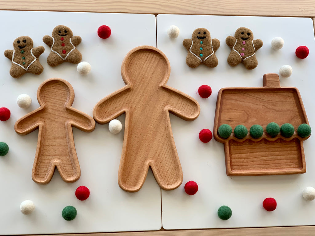 Set of three natural wooden sensory trays shaped like gingerbread people and a house surrounded by felt balls and gingerbread figures