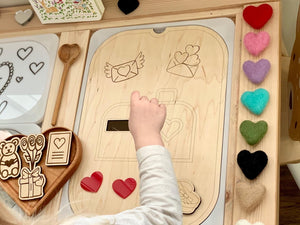 Child placing felt heart into wooden love mailbox insert on Flisat table top with heart decorations and wooden toys