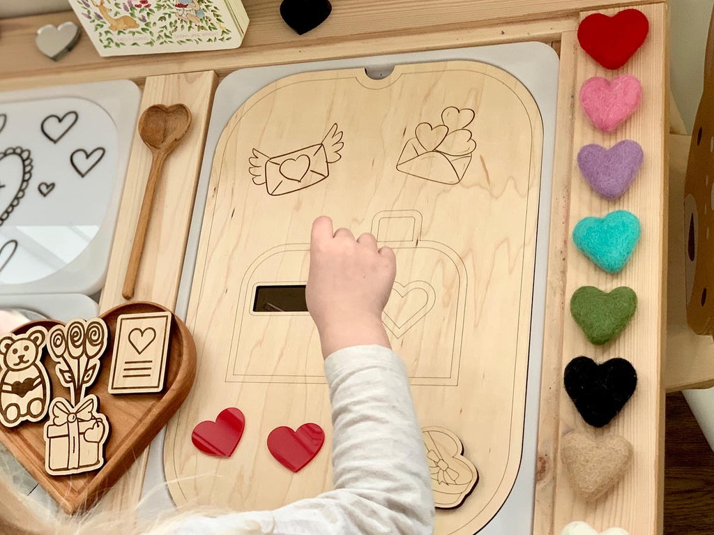 Child placing felt heart into wooden love mailbox insert on Flisat table top with heart decorations and wooden toys