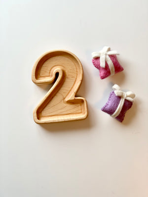 Natural wooden number plate shaped as number 2 with two small wrapped felt sensory toys on white background