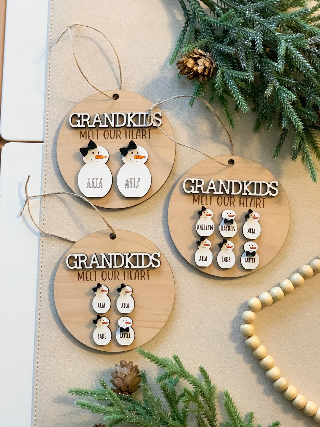 Set of three wooden round Christmas ornaments with snowman figures and personalized grandkids names on natural twine