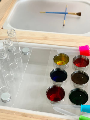 Clear acrylic test tube Flisat insert with metal lids, metal cups filled with colorful liquids, and droppers on wooden table