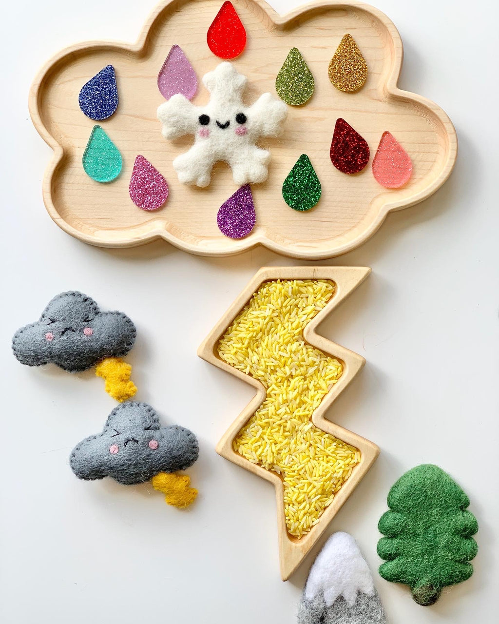 Natural wooden cloud-shaped sensory tray with colorful felt raindrops and smiling snowflake on wood grain background