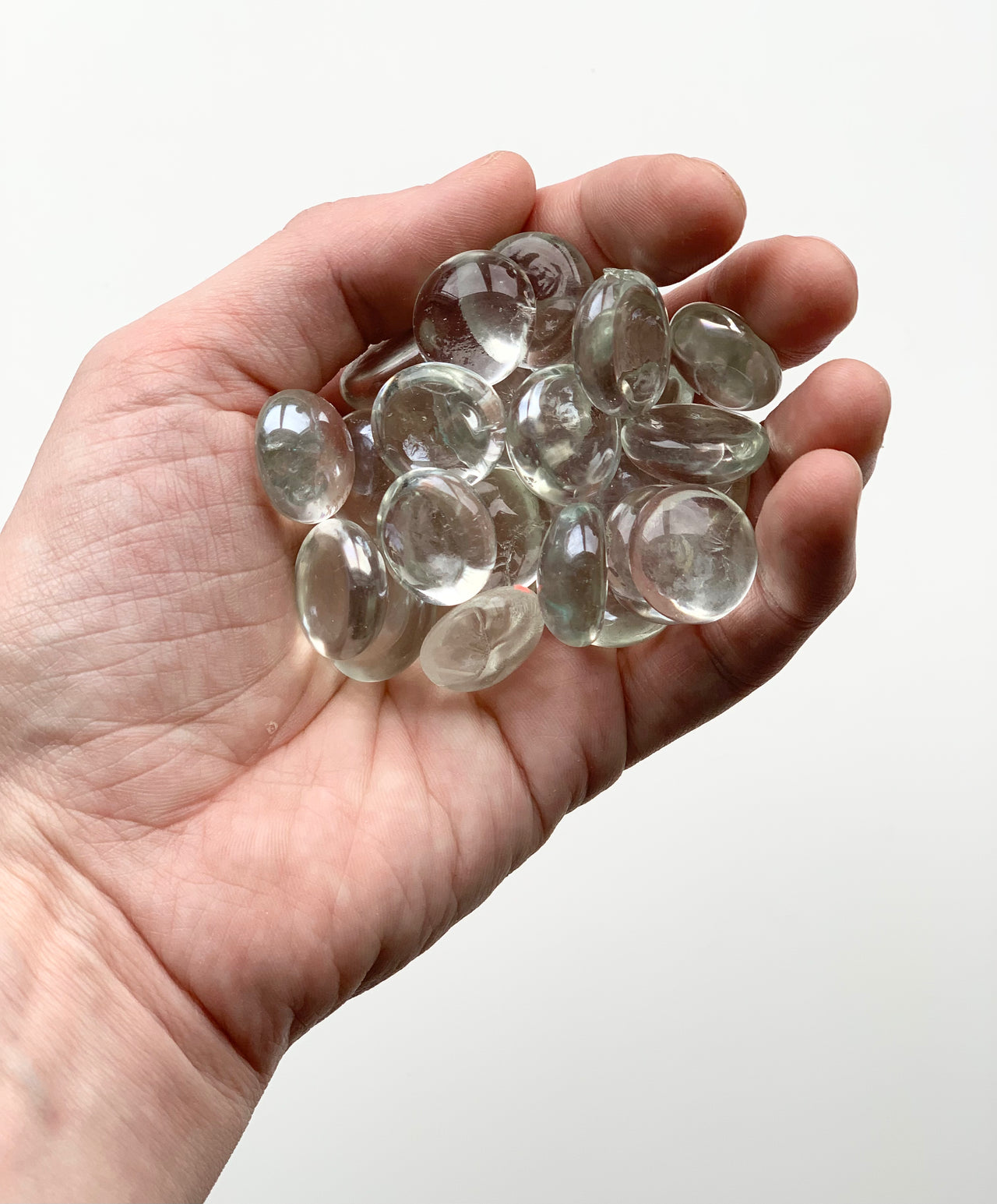 Hand holding clear round glass treasure gems with smooth shiny surfaces on white background