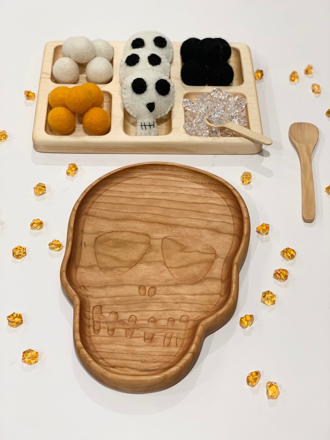 Natural wooden skull-shaped plate with matching sensory tray holding felt balls and clear beads on white surface