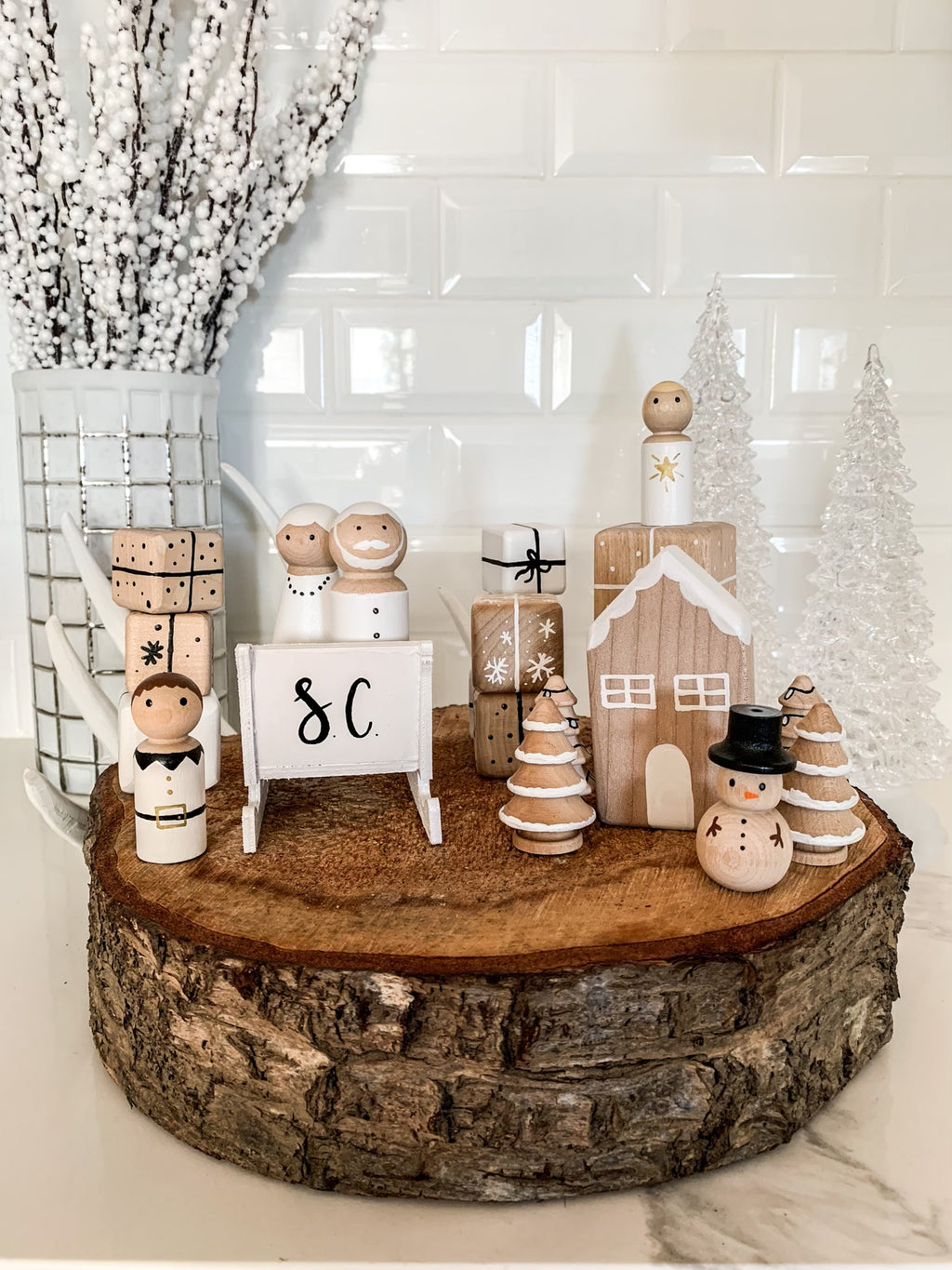 Made-to-order wooden Christmas peg dolls including snowman, presents, trees, and house displayed on rustic wood slice