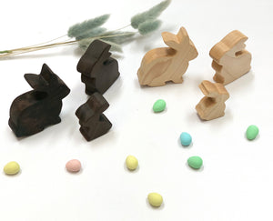 Set of dark and light natural wooden toy bunnies arranged with pastel colored eggs and dried grass on white surface