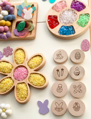 Wooden Easter memory game discs with engraved spring-themed icons arranged next to flower-shaped tray filled with colored rice