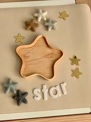 Wooden star-shaped tray surrounded by neutral felt stars and gold star confetti on beige surface with white letters spelling star