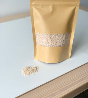 Brown kraft resealable pouch filled with pale pink sensory filler rice spilling onto white table surface