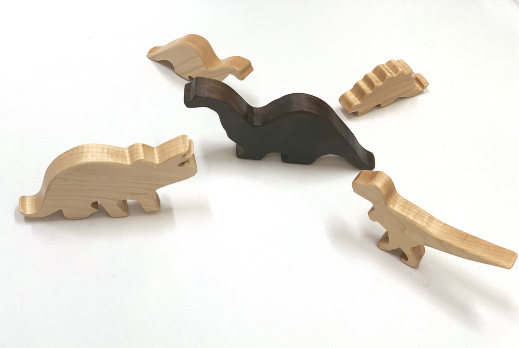 Set of five handcrafted wooden dinosaur toy figurines in natural and dark wood tones on white background