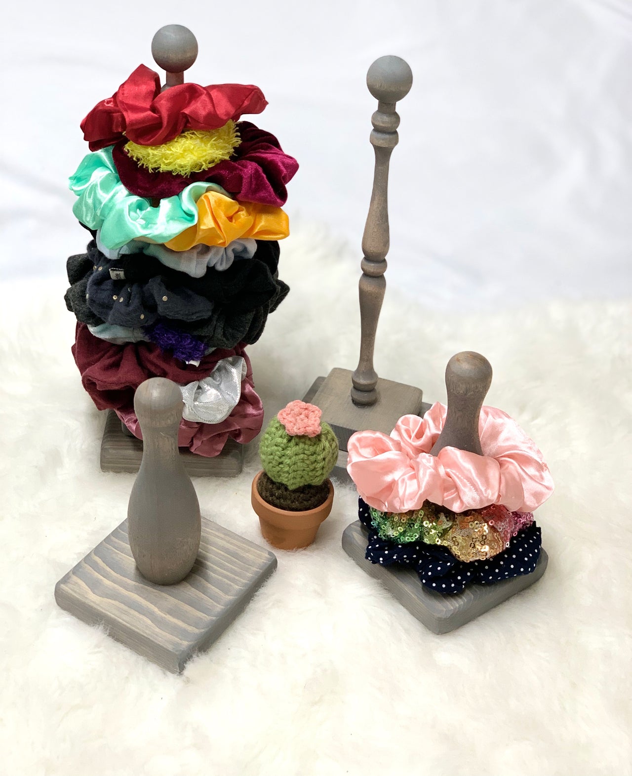Large natural wooden scrunchie holder stacked with colorful velvet and satin scrunchies on white fuzzy surface