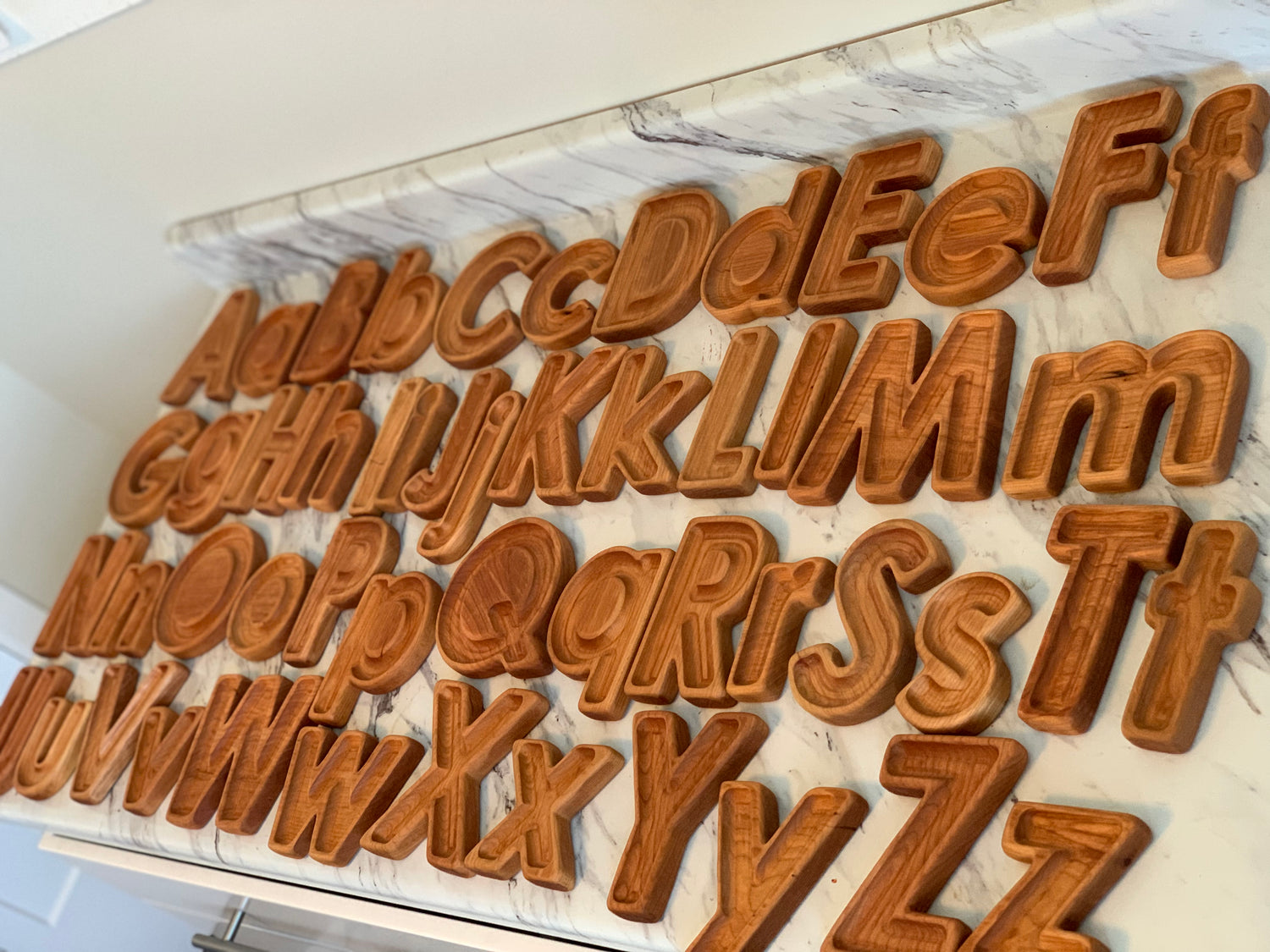 Natural wooden alphabet letters in uppercase and lowercase arranged on marble surface for sensory play