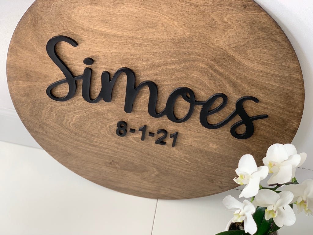 Oval wooden 3D round sign with black last name letters and date on smooth natural wood grain background