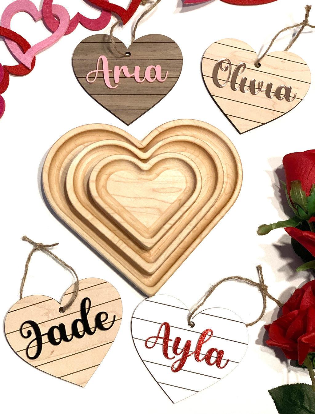 Heart shaped wooden name tags with various names in script font surrounding nested plain wooden heart trays on white background