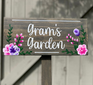 Large custom wooden garden sign with white cursive letters and pink and purple floral illustrations on stained wood background