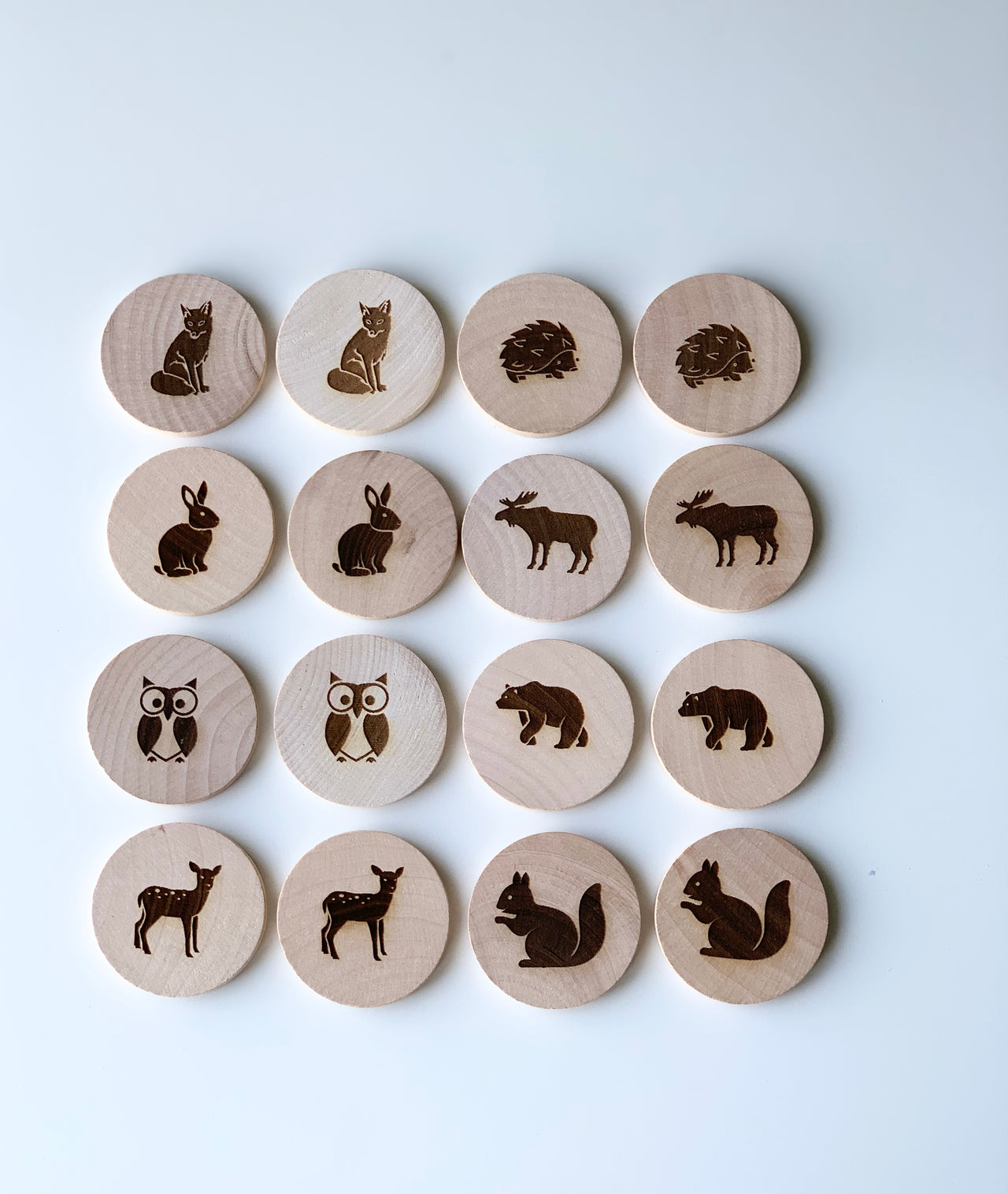 Natural wooden memory game discs with engraved woodland animal pairs on white background arranged in rows