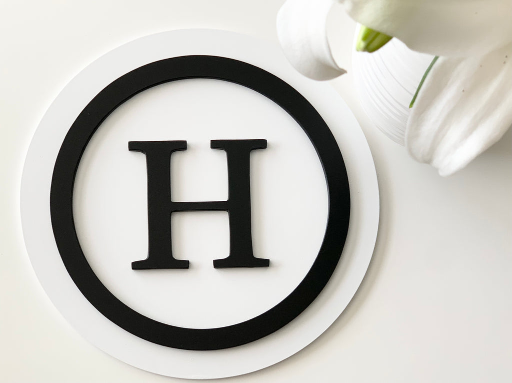 3D monogram round sign with black letter H and circle on white layered MDF background near white flower