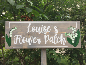Large custom wooden garden sign painted gray with white cursive letters and lily of the valley floral illustrations on wood grain background