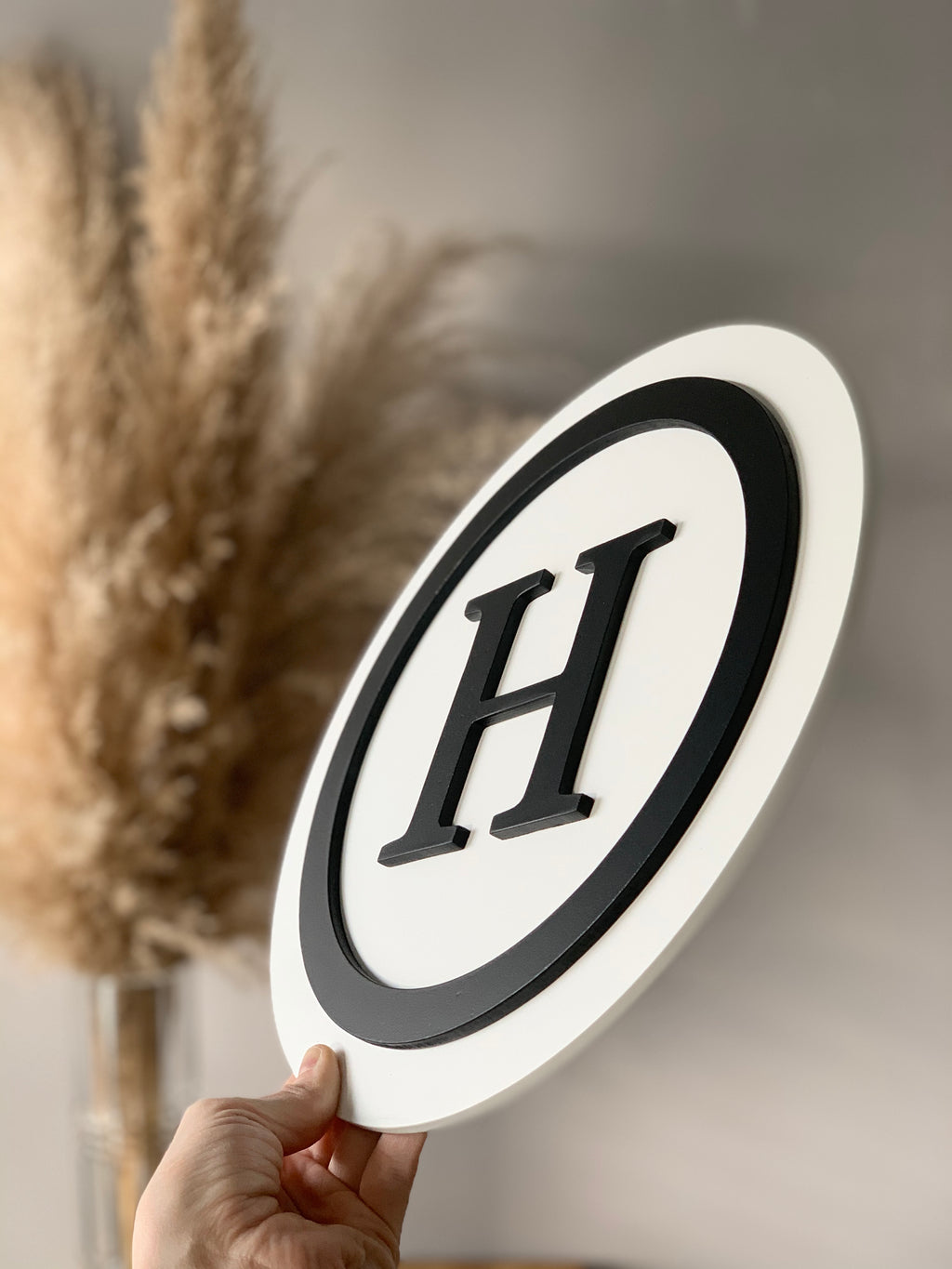 Round 3D monogram sign with black letter H and outline on white layered MDF background held by hand