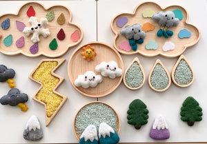Wooden sensory tray set with weather-themed felt clouds, raindrops, lightning bolt, trees, and mountains on white background