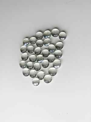 Clear glass treasure gems scattered in a cluster on white surface with light reflections on smooth rounded stones