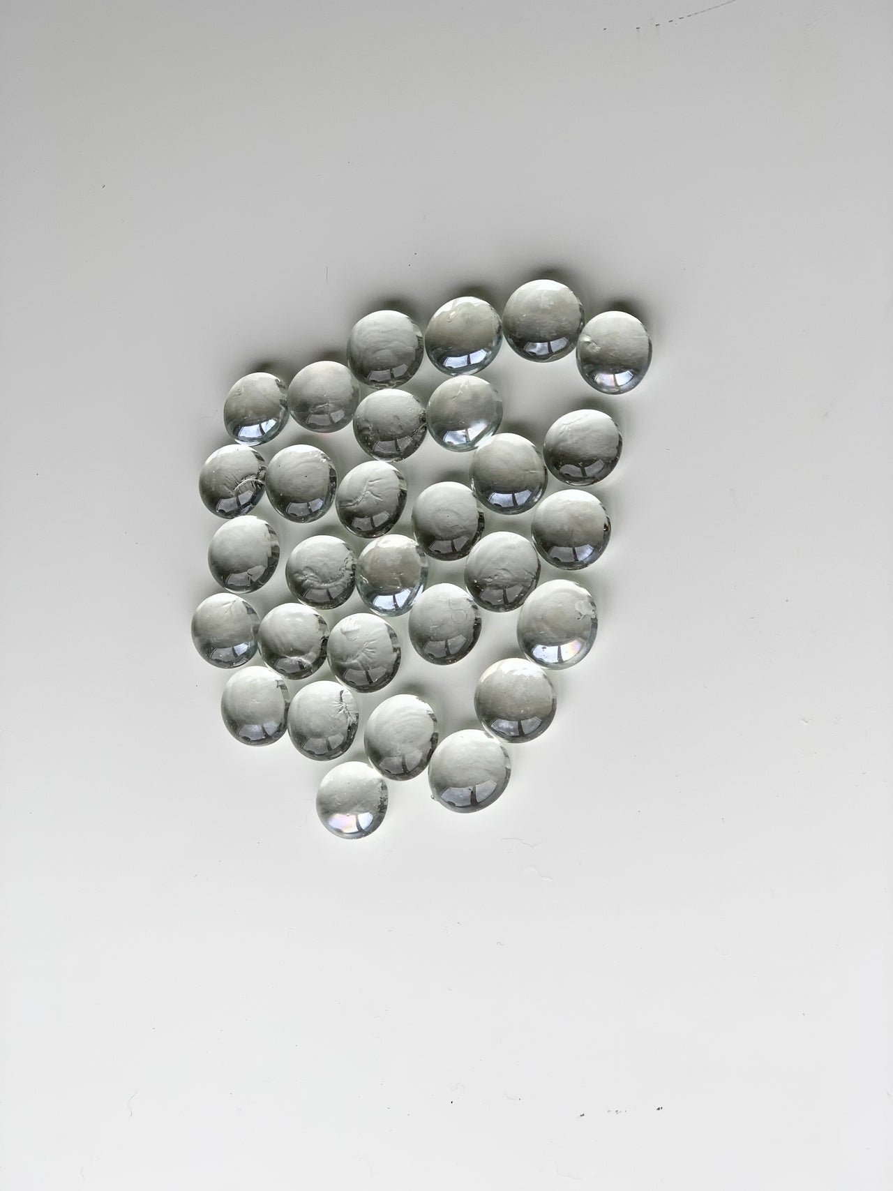 Clear glass treasure gems scattered in a cluster on white surface with light reflections on smooth rounded stones